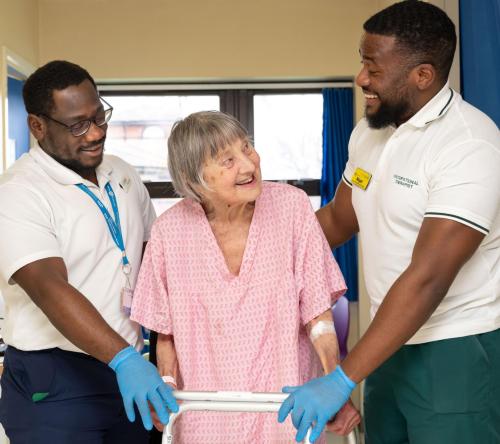 Patient with a walking frame being helped by two members of staff on either side of her
