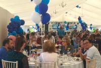 A wide shot with lots of staff at tables in the marquee for our afternoon tea. In the foreground, a man wearing glasses is looking at the camera and gives a thumb up gesture.